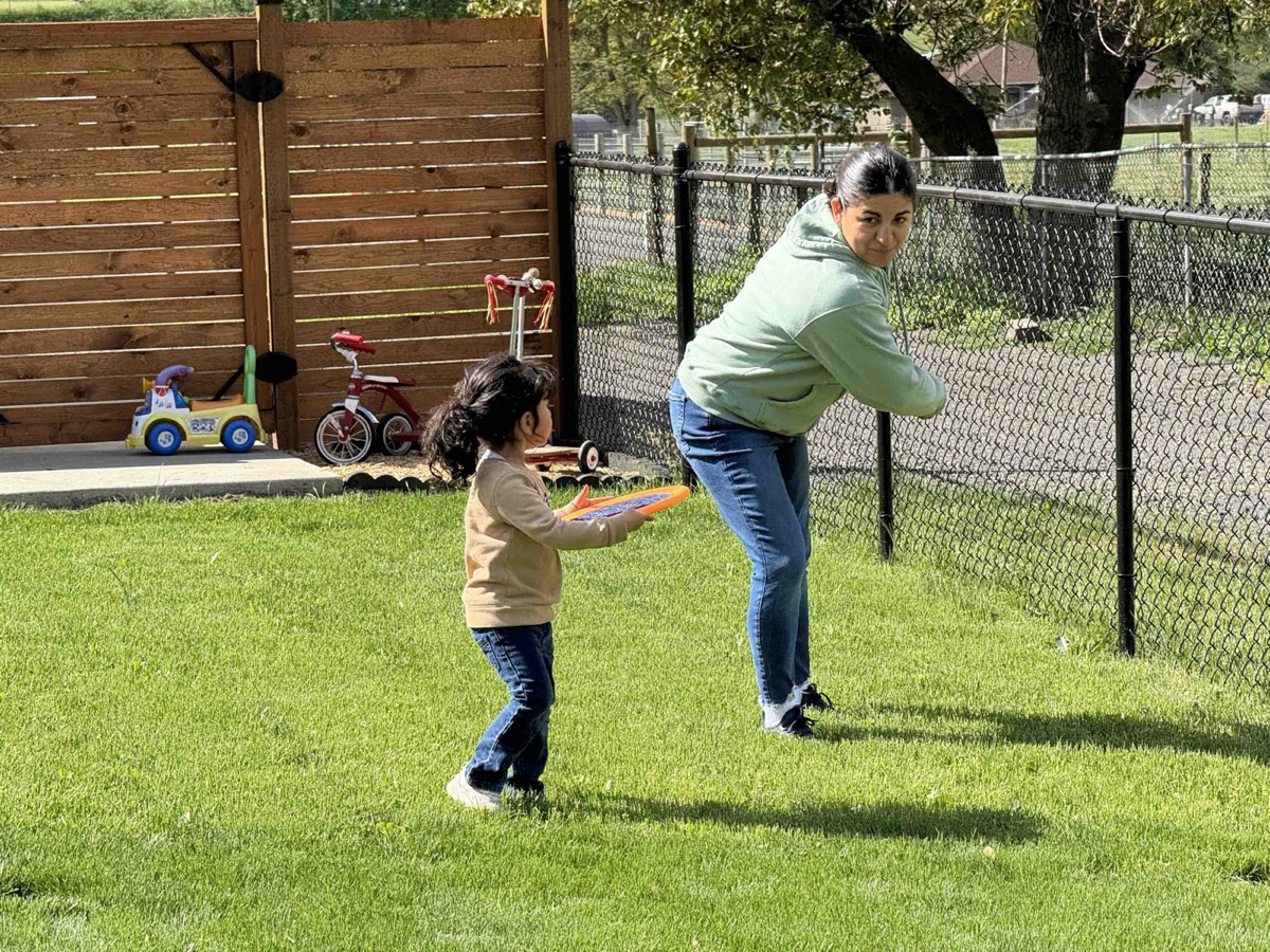 A teacher and a toddler playing frisbee on the lawn