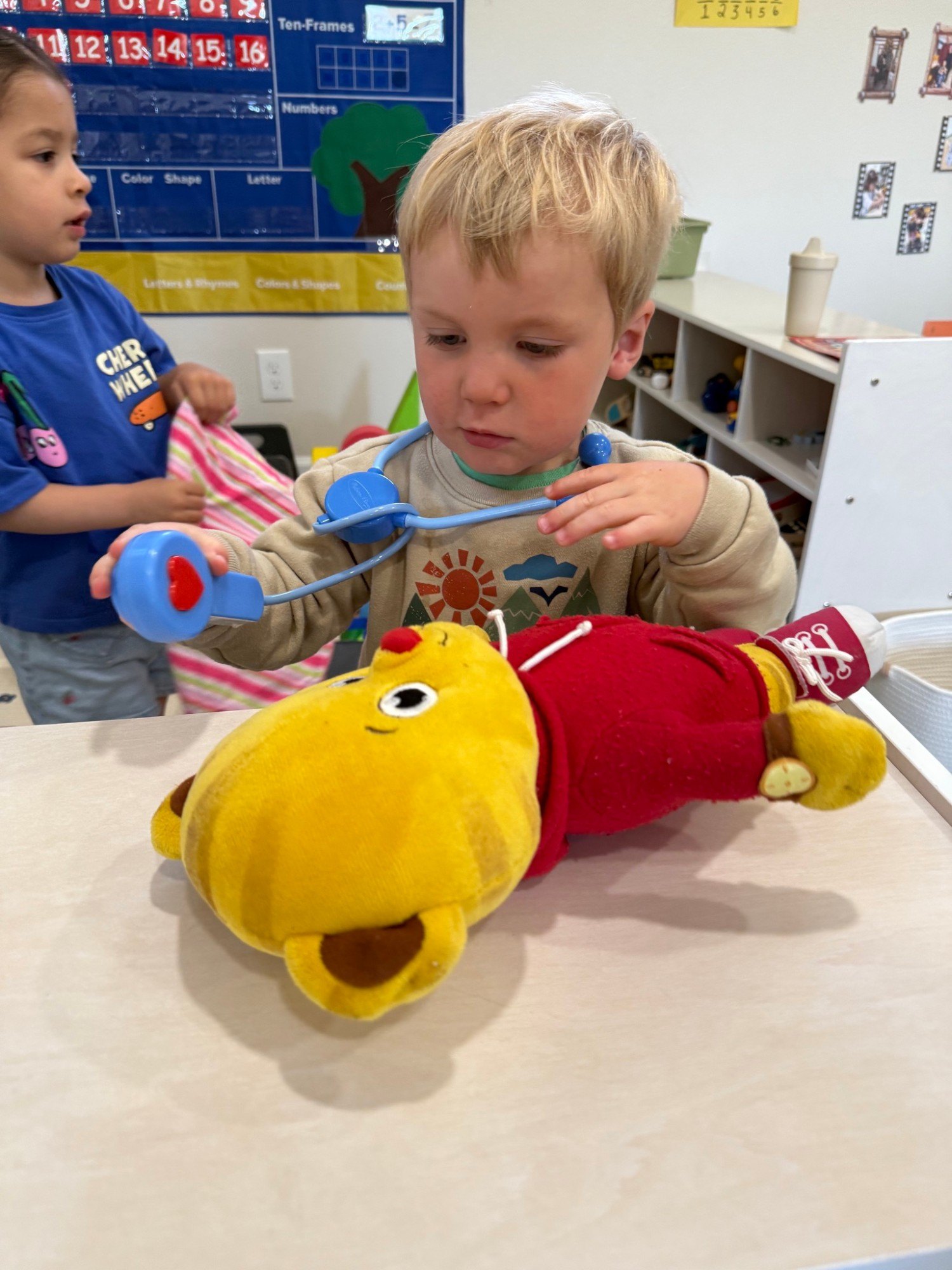 A toddler using a toy stethoscope on a stuffed tiger