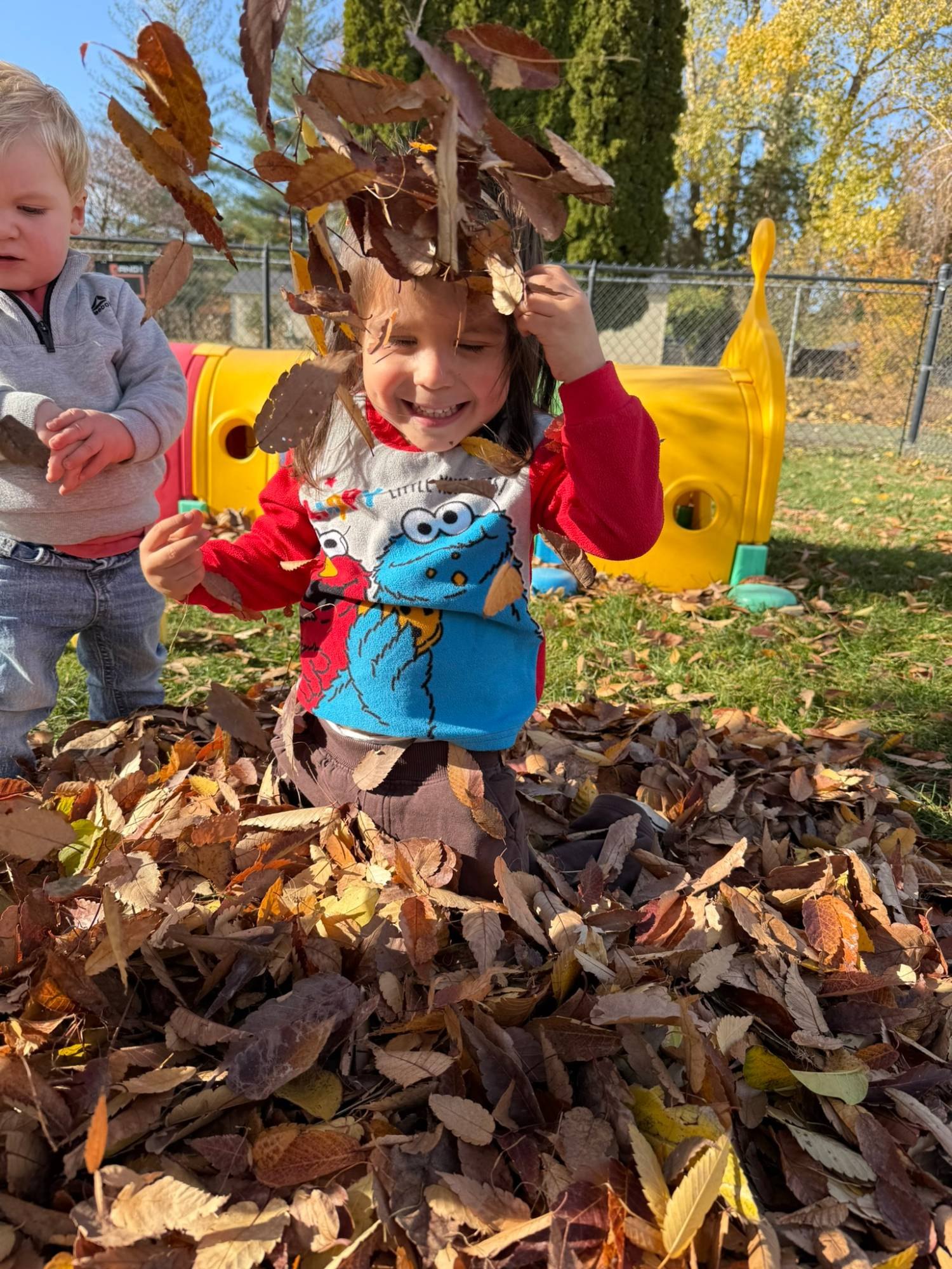 A laughing child tossing dry leaves in a big pile in the backyard