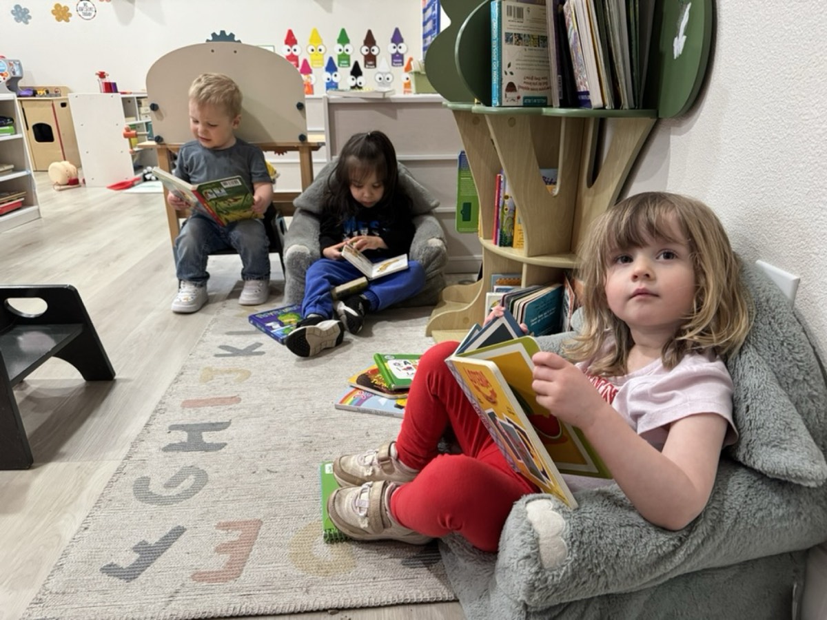 Children reading books on soft chairs by a bookshelf